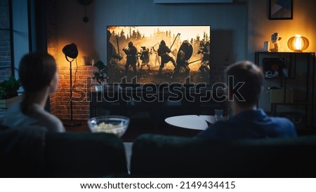 Authentic Couple Spending Time at Home, Sitting on a Couch and Watching Latest Blockbuster on Flat Screen Television Set. Man and Woman Streaming Movie or Show Using Home Cinema System.