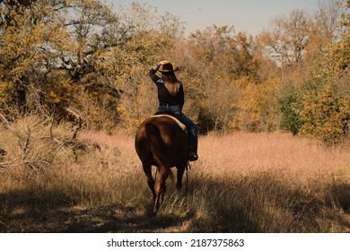 Authentic Cowgirl Riding Horseback Through Rural Ranch Pasture During Fall Season In Texas, Western Industry.