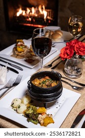 An authentic dinner table set next to a cozy fire place, a curry and a glass of red wine to enjoy