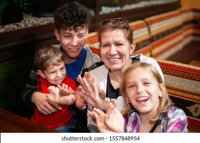 Authentic Family Photo - Mother With Three Kids Genuinely Laughing And Clapping Hands, Having Fun And Waiting For Pizza At The Cafe