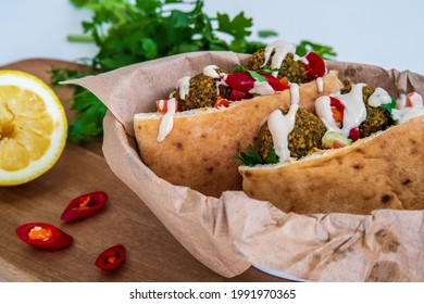 Authentic Fresh Falafel Balls Inside Of Two Halves Of Pita Bread Sandwich With Chopped Salad, Red Hot Peppers, Lemon, A Drizzle Of Tahini Sauce. Chickpea Falafel In A Fluffy Pita On A Wooden Board