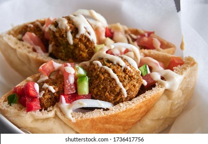 Authentic fresh falafels balls inside of two halves of pita bread sandwich with chopped salad and drizzle of tahini sauce on top, close-up of chickpea falafel in a gluten-free pita