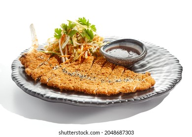 Authentic German schnitzel with cabbage salat and sauce on black plate. Breaded meat - popular restaurant dish Viennese schnitzel. Thin slice of meat breaded with vegetables salad on white background