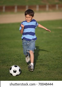 Authentic Happy Latino Boy Playing With Soccer Ball In Field Wearing Blue Striped Tee Shirt.