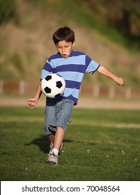 Authentic Happy Latino Boy Playing With Soccer Ball In Field Wearing Blue Striped Tee Shirt.