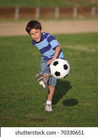 Authentic Happy Latino Boy Playing With Soccer Ball In Field Wearing Blue Striped Tee Shirt.