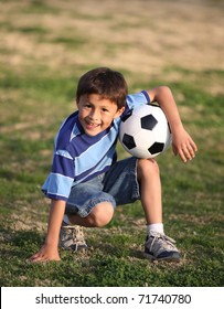 Authentic Happy Latino Boy With Soccer Ball In Field Wearing Blue Striped Tee Shirt.