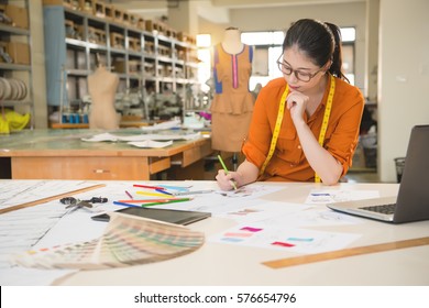 Authentic Image Of Asian Fashion Woman Designer Drawing Design Sketch Working In Her Manufacturing Office Studio. Profession And Job Occupation Concept.
