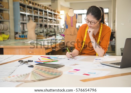 authentic image of asian fashion woman designer drawing design sketch working in her manufacturing office studio. profession and job occupation concept.