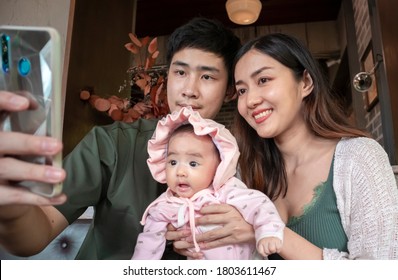 Authentic Image In Camera Auto Mode : Asian Young Parents And Baby Looking At Phone. Concept Of Family Lifestyle, Parenthood, Technology. Family Communication, Family Connection, Facetime.