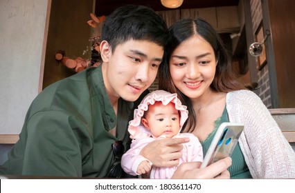 Authentic Image In Camera Auto Mode : Asian Young Parents And Baby Looking At Phone. Concept Of Family Lifestyle, Parenthood, Technology. Family Communication, Family Connection, Facetime.