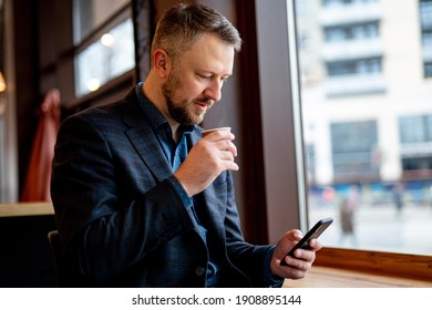 Authentic image of a pensive businessman in a coffee shop. Businessman in dark suit having break surfing internet on the phone. - Shutterstock ID 1908895144