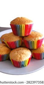 Authentic, imperfect rustic-looking cupcakes featuring vibrant rainbow layers and cracked surfaces, symbolizing real home baking for Pride Month. Close-up of basic, easy-to-make rainbow celebration cupcakes with naturally cracked tops, perfect for casual cooking blunders, love, and diversity themes.  Charm of vanilla, citrus, orange, lemon, plain cupcakes with cracked tops and rustic appearance in colorful rainbow wrappers. A ceramic plate filled with freshly baked French vanilla muffins in vibrant rainbow-colored paper wrappers for Gay Pride week celebrations.