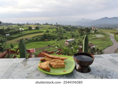 Authentic Indonesian breakfast: Crispy banana fritters and traditional Kopi Kawa (coffee leaf tea) with breathtaking views of emerald rice terraces and misty mountains in West Sumatra. A perfect blend - Powered by Shutterstock