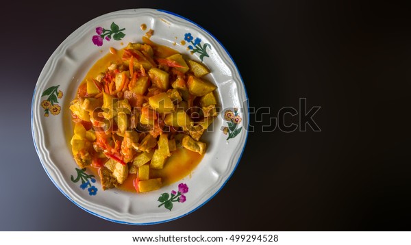 Authentic Indonesian food from family street\
restaurant. Mixed tofu potato and tempe cooked in tomato and carrot\
sauce. Plate isolated on plain dark background with section for\
text. Delicious meal.