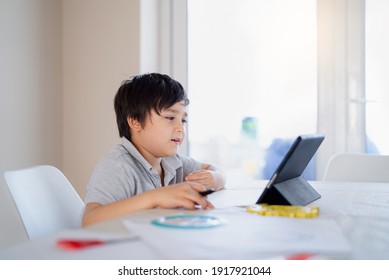 Authentic Kid Doing Online Homework With Friends At Home, Child Using Tablet For Home Learning, School Boy Studying Online Zoom Video Call With Teacher, E-learning Or Homeschooling Education Concept