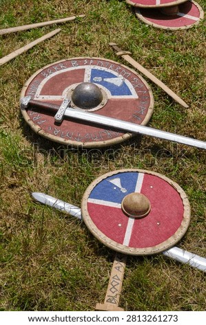 Authentic looking Viking age weaponry including round shields and long swords are displayed on a green grassy field for historical reenactment.