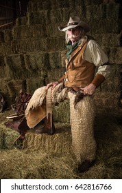 Authentic old west cowboy portrait with wooly chaps, pistol, cowboy hat, leather vest, bandanna in stable