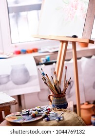 Authentic Paint Brushes Still Life On Table In Art Class School As Drawing Course. Cropped Shot Of Group Of Brush In Clay Jar. Discounts On Goods For Artists. Easel For Still Lifes.