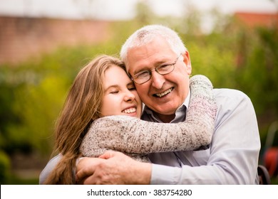 Authentic photo of smiling grandfather hugging with his teenage granddaughter outdoor in nature