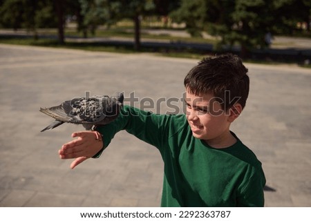 Authentic portrait of adorable multi ethnic pre teen boy, smiling and having fun while standing in the square and feeding rock pigeons. Carefree and happy hildhood. People and wild animals concept