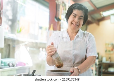 Authentic Portrait Asian Elderly Woman. Cooking With Love For Family Dinner Food Concept. Local Traditional Thai Style Indoors Kitchen At Home. Eye Looking At Camera.