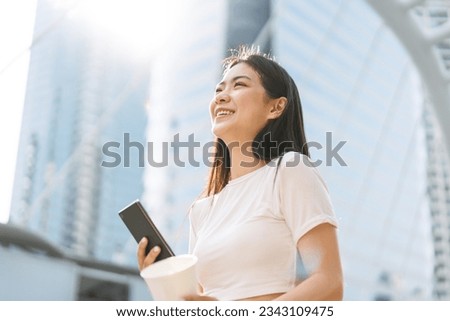 Authentic portrait beautiful asian woman urban lifestyles. Long hair happy smile attractive face looking up. Hand with smartphone and coffee cup. Standing at outdoors. City building background.