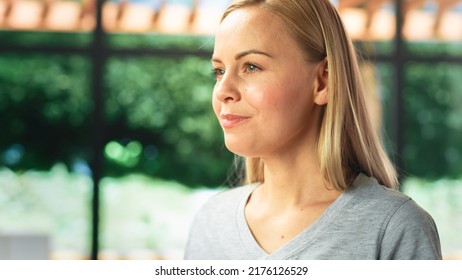 Authentic Portrait Of Beautiful Young Female In Kitchen Room At Home Looking Thoughtfully At Her Backyard. Attractive Blond Woman Poses For Camera And Smiles. Happy Person With Healthy Lifestyle.