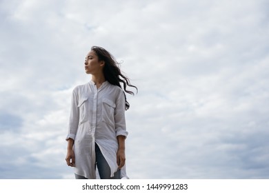 Authentic Portrait Of Christian Woman Breathing Fresh Air, Thinking, Makes Important Life Decisions. Asian Girl With Emotional Face Standing On Background Of Clouds. Faith In God. Religion Concept 