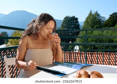 Authentic portrait of a curly pretty woman drinking orange juice and reading magazine, taking her breakfast on the balcony on a beautiful sunny summer day in Italian village. People. Travel Lifestyle - Powered by Shutterstock