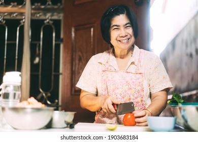 Authentic Portrait Of Happy Smile Asian Elderly Woman. Cooking With Love For Family Dinner Food Concept. Local Traditional Thai Style Outside Kitchen At Home. 