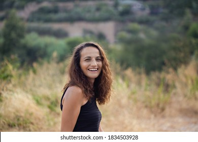 Authentic Portrait Of A Laughing Female In Her Thirties With Wavy Hair, Posing Outdoors And Wearing Summer Outfit. Negative Space.