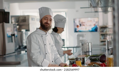 Authentic Portrait Of Professional Chef Preparing Celery For Gourmet Dish In Restaurant Kitchen, Using Organic Ingredients. Smiling Man Cooking Culinary Recipe Meal For Gastronomy. Handheld Shot.