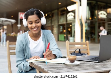 Authentic portrait of smiling Indian student wearing wireless headphones using laptop computer studying, taking notes, exam preparation, online education concept - Shutterstock ID 2167413261