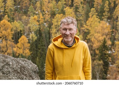An authentic portrait of a smiling unshaven male traveler in a yellow hoodie on top of a mountain, against the background of an autumn forest. Selective focus. Close-up. Sustainable environment. - Shutterstock ID 2060760710