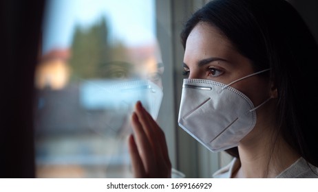 Authentic Portrait Of An Young Woman Wearing A Protective Mask Is Looking Through A Window. Concept Of Pollution, Environment, Protection, Virus Transmission, Breathing,safety, Quarantine, Covid-19