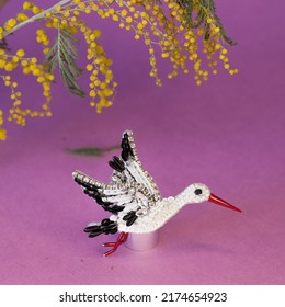 Authentic Representation Of Handmade Craft Beaded Stork Bird As Accessory Brooch Pin Isolated Overt Pink Background With Mimosa Flowers On Top