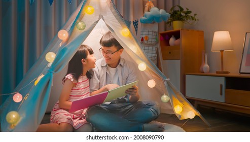 Authentic Shot Of Asian Girl And Her Father Enjoy Their Fun Time With Story Book In The Evening At Home