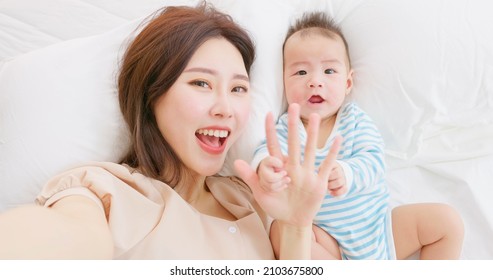 Authentic Shot Of Asian Mother And Her Baby Take Selfie By Mobile Phone When Lying On Bed In Close Up