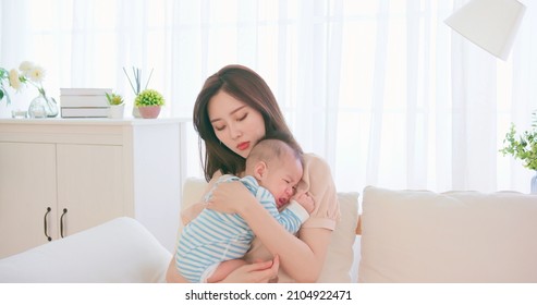 authentic shot of asian mother holding her crying baby on sofa has postpartum depression