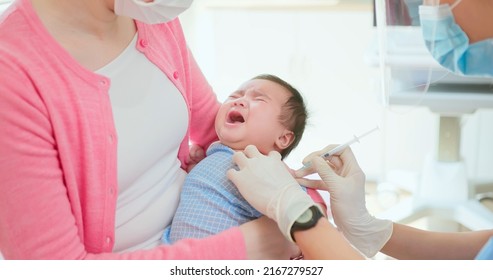 Authentic Shot Of Asian Mother And Infant In Pediatrics Clinic - Doctor Wearing Face Mask Inject Vaccine To A Baby Who Is Hold By Mom