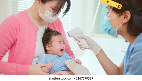authentic shot of asian mother and infant in pediatrics clinic - doctor examine crying baby health and using thermometer to check body temperature on forehead