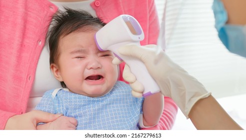 Authentic Shot Of Asian Mother And Infant In Pediatrics Clinic - Doctor Examine Crying Baby Health And Using Thermometer To Check Body Temperature On Forehead