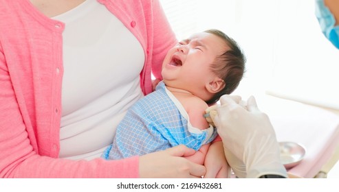Authentic Shot Of Asian Mother And Infant In Pediatrics Clinic - Doctor Wearing Face Mask Inject Vaccine To A Baby