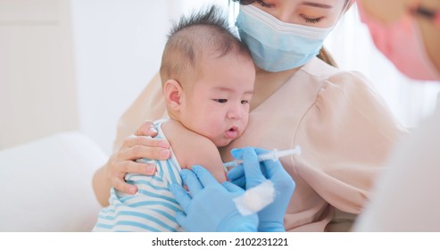 authentic shot of asian mother wearing face mask holds her baby for vaccinated by doctor