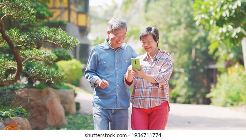 Authentic Shot Of Asian Senior Couple Are Wandering On Walkway And Sharing Social Media Content By Mobile Phone