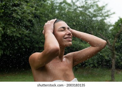 Authentic shot of carefree young woman feeling free and smiling while refreshing under the rain on background of green trees. Concept of life, freedom, nature, adventure, purity,water, tropical,exotic
