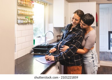 Authentic shot of happy married homosexual female gay couple expecting a baby and eating healthy apple together in the kitchen - lesbian couple at home enjoying life together