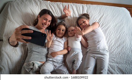 Authentic shot of happy mother with her kids are making a selfie or video call to father or relatives in a bed. Concept of technology, new generation,family, connection, parenthood, authenticity