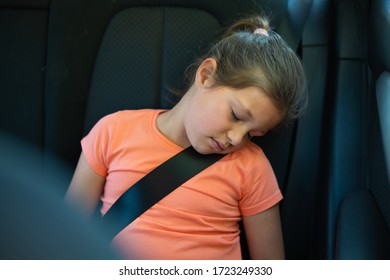 Authentic Shot Of A Preschooler Girl Is Sleeping In A Backseat Of A Car Locked With Safety Belt During Traveling With Family.